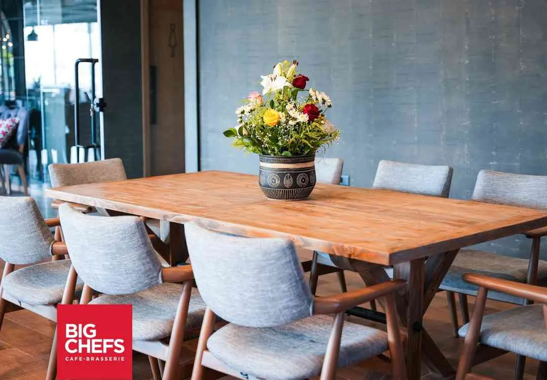 A long wooden dining table set with flowers and grey upholstered chairs at BigChefs Tripoli